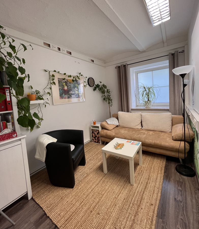 Therapiezimmer mit Sofa, Sessel, Tisch und Pflanzen.
